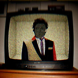 A CRT television set showing a man wearing a multicolored suit with television static obscuring his face