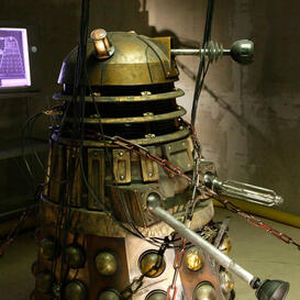 A worn-down Dalek bound in chains in a dimly lit room