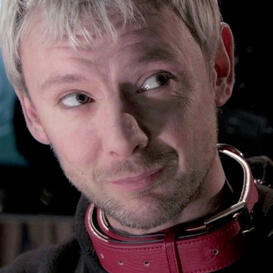 A humanoid with short blond hair wearing a black hoodie and red collar
