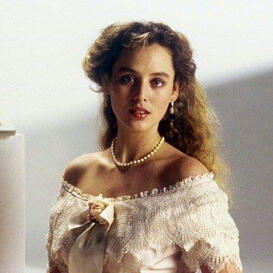 A woman with long curly hair wearing a white dress and looking at the camera