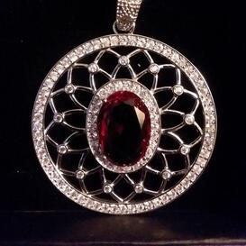 A circular silver necklace with a large red gemstone set in the middle