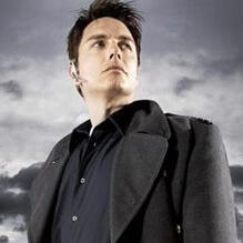 A man with short dark brown hair in a black jacket and navy blue button up