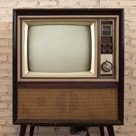 An old brown television set with switches and dials to the right and a speakerbox underneath